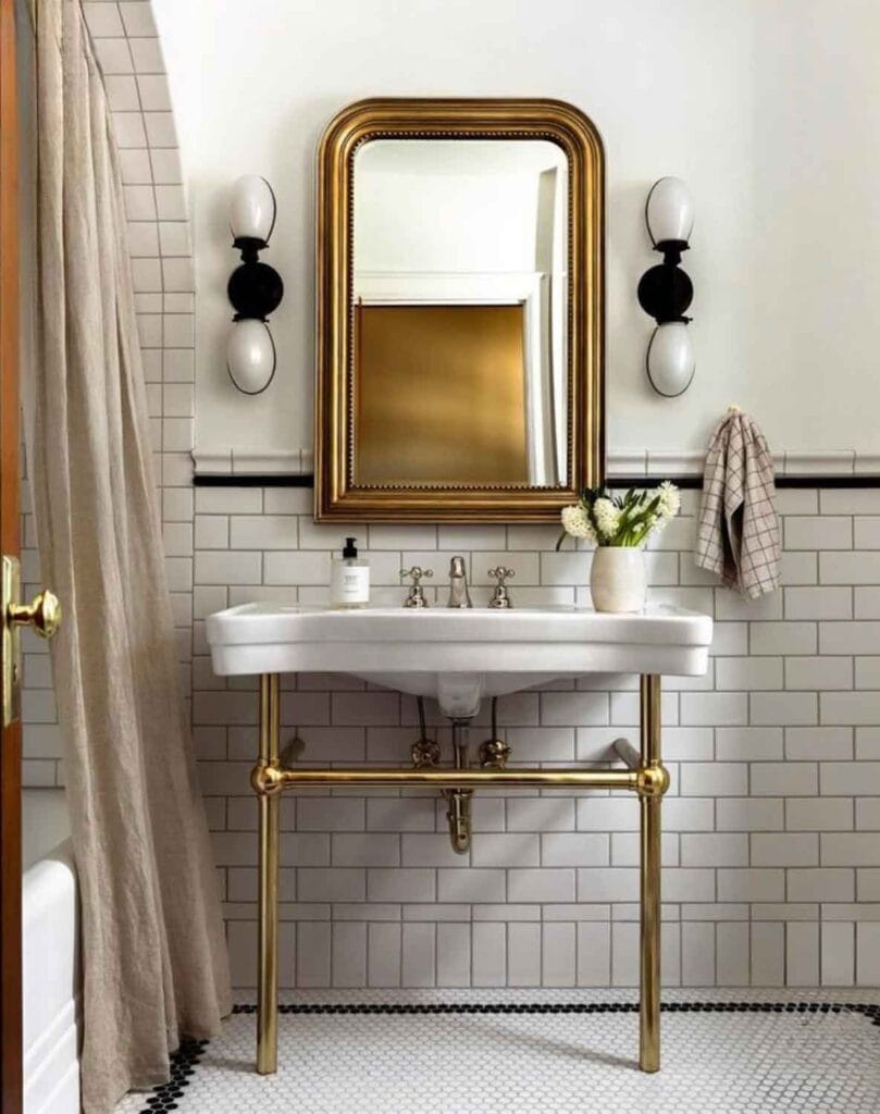 Sink with brass base, brass mirror, black and white sconces.