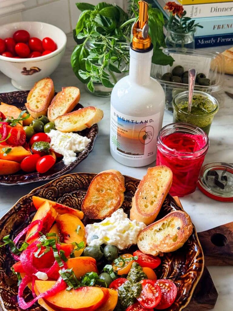Brown plate with peaches, cheesem tomatoes. Jars of pickled red onions, prest, olive oil.