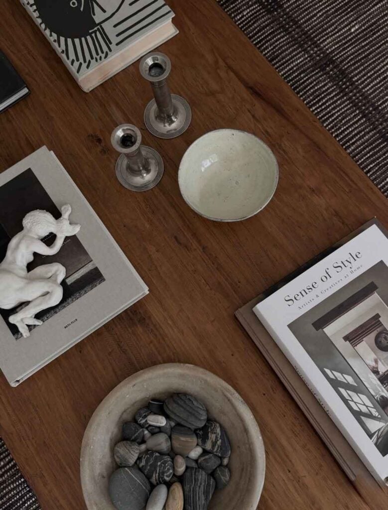Coffee table with bowl of interesting stones, silver candle holders, small bowl, books.
