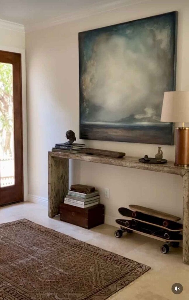 Console table with large scale painting, skate boards underneath, lamp.