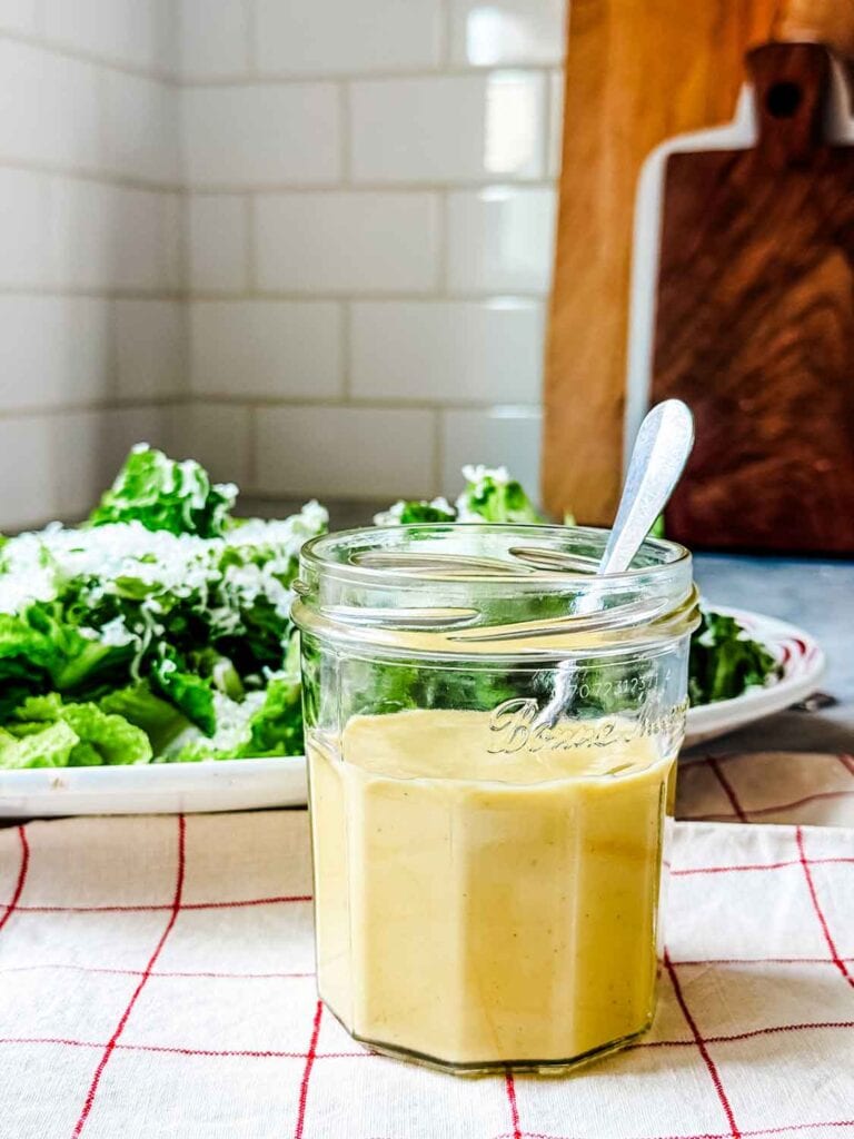 Jar of caesar salad dressing with a spoon in the jar.