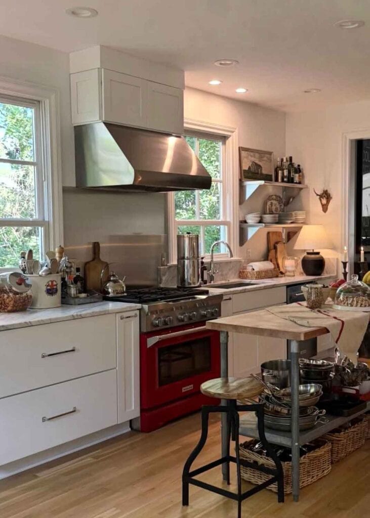 Red kitchen range with stainless hood, kitchen island, white cabinets. 