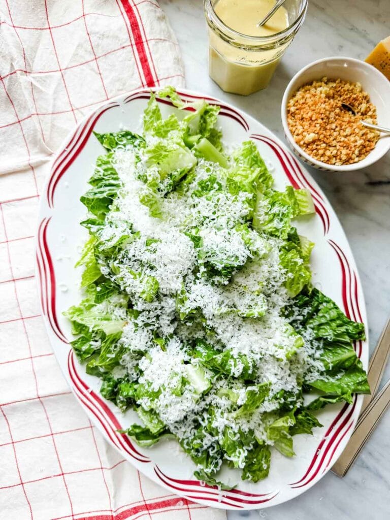 Caesar salad on platter with a red design on the rim, jar of salad dressing, bowl of panko breadcrumbs