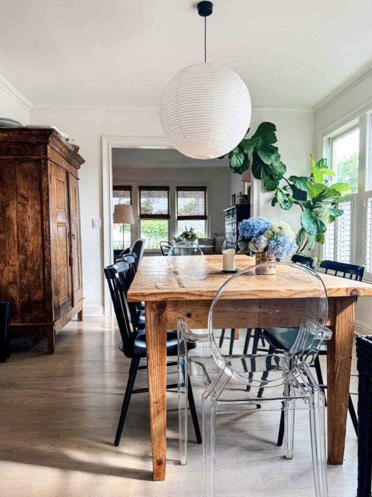 Farm table with black side chairs, ghost chair at ends, plant in corner, hydrangeas in vase.