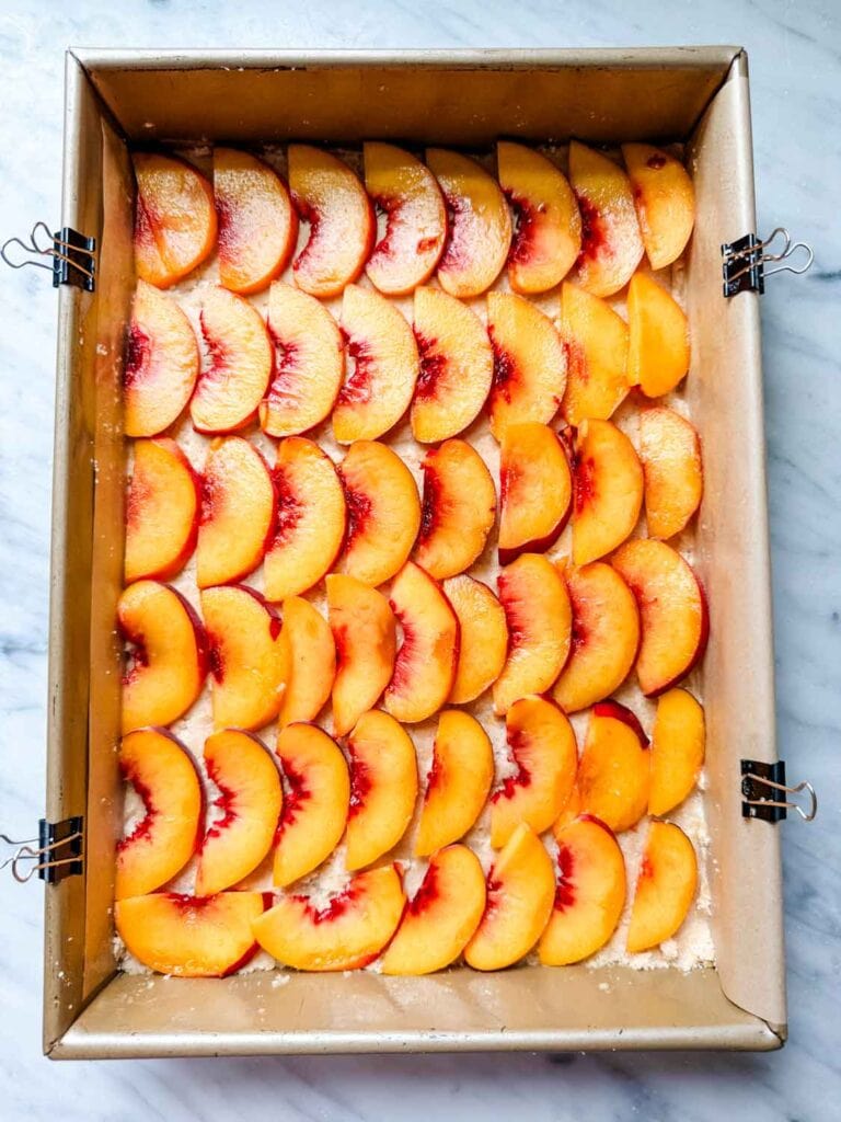 The sliced peaches are lined evenly on top of the shortbread crust before baking.