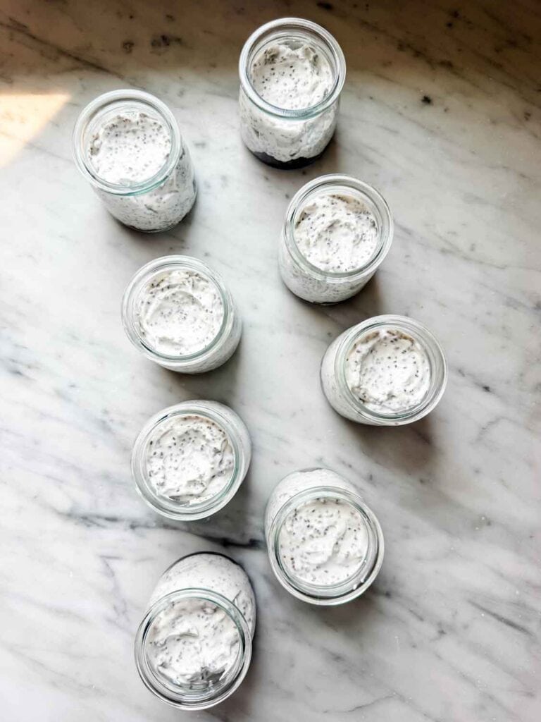 Small jars are filling with blueberry compote and chia seeds mixed with Greek yogurt, are sitting on a kitchen counter.