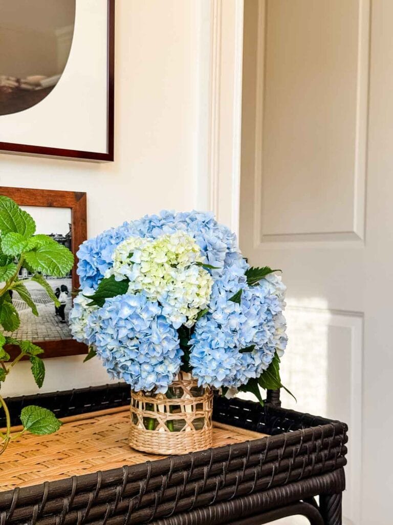 Blue hydrangeas in rattan vase on rattan side cart.