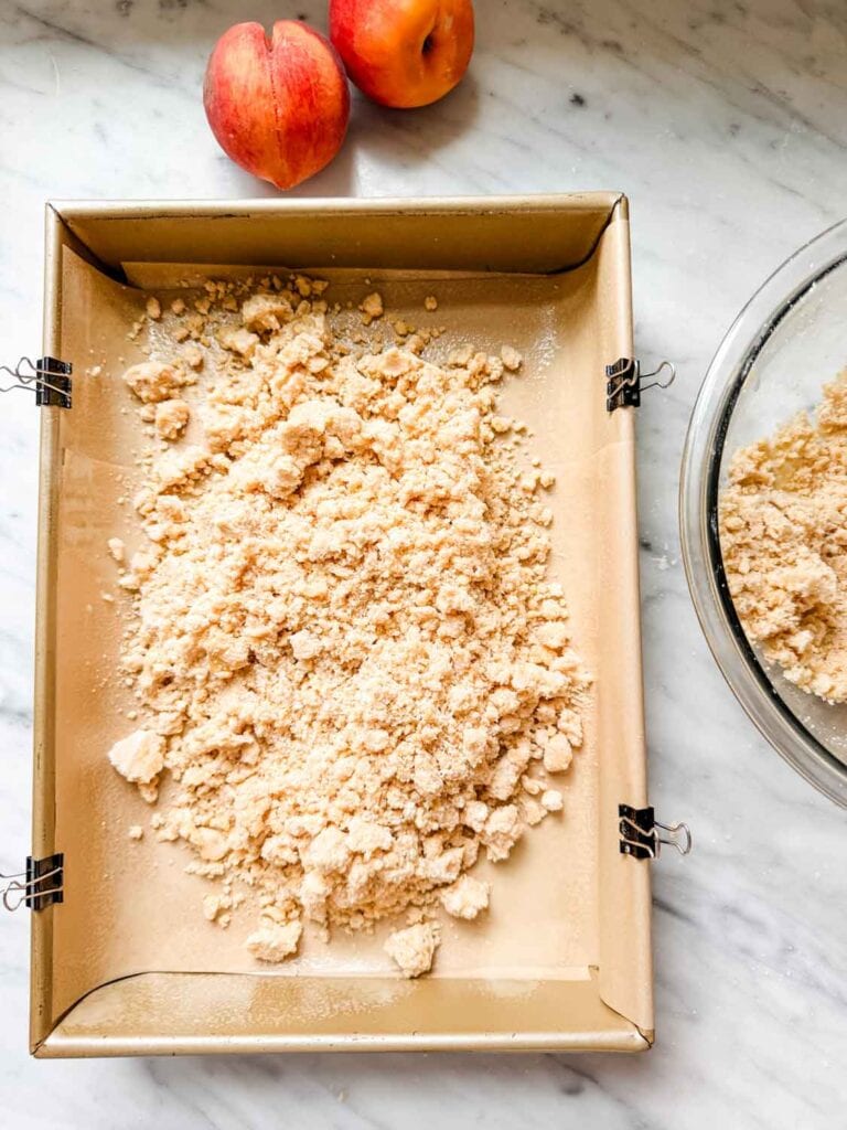 The crumbly shortbread dough is dumped into the baking pan and ready for pressing down to form the crust.