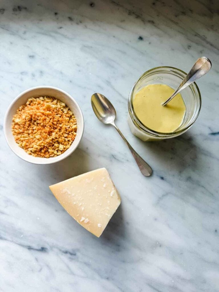 Jar of caesar salad dressing with a spoon in the jar, next to a bowl of toasted panko, and parmesan cheese.