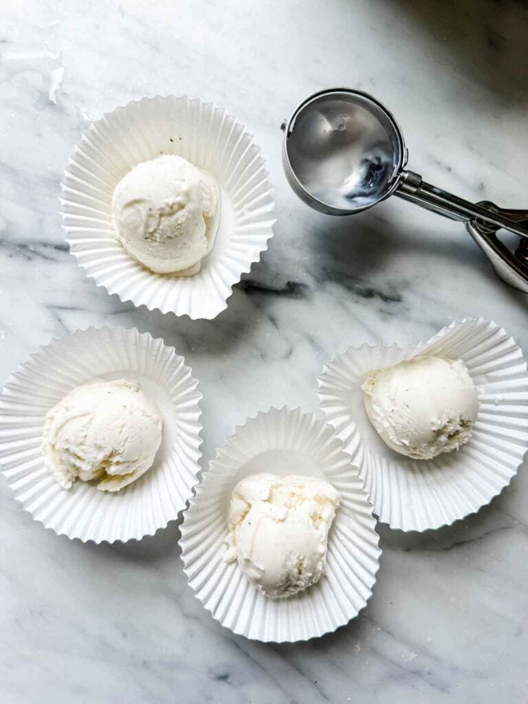 Vanilla ice cream in white cupcake liners with ice cream scoop. 