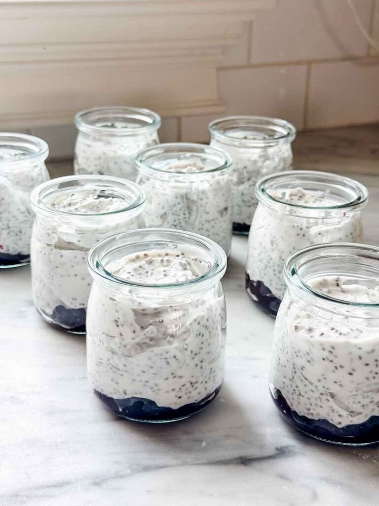 Small glass jars are filled with blueberry compote and Greek yogurt mixed with Kefir and chia seeds.