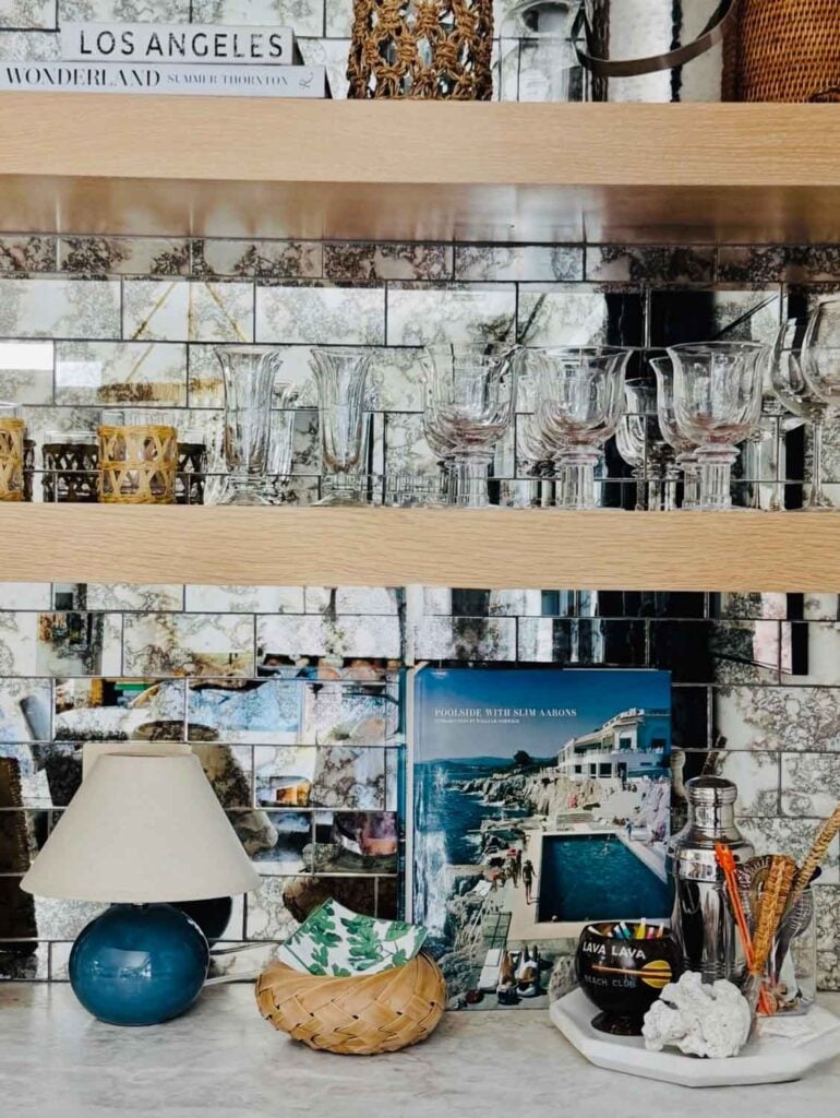 A bar with mirrored subway tile, small lamp, tray holding drink items, small basket holding napkins.