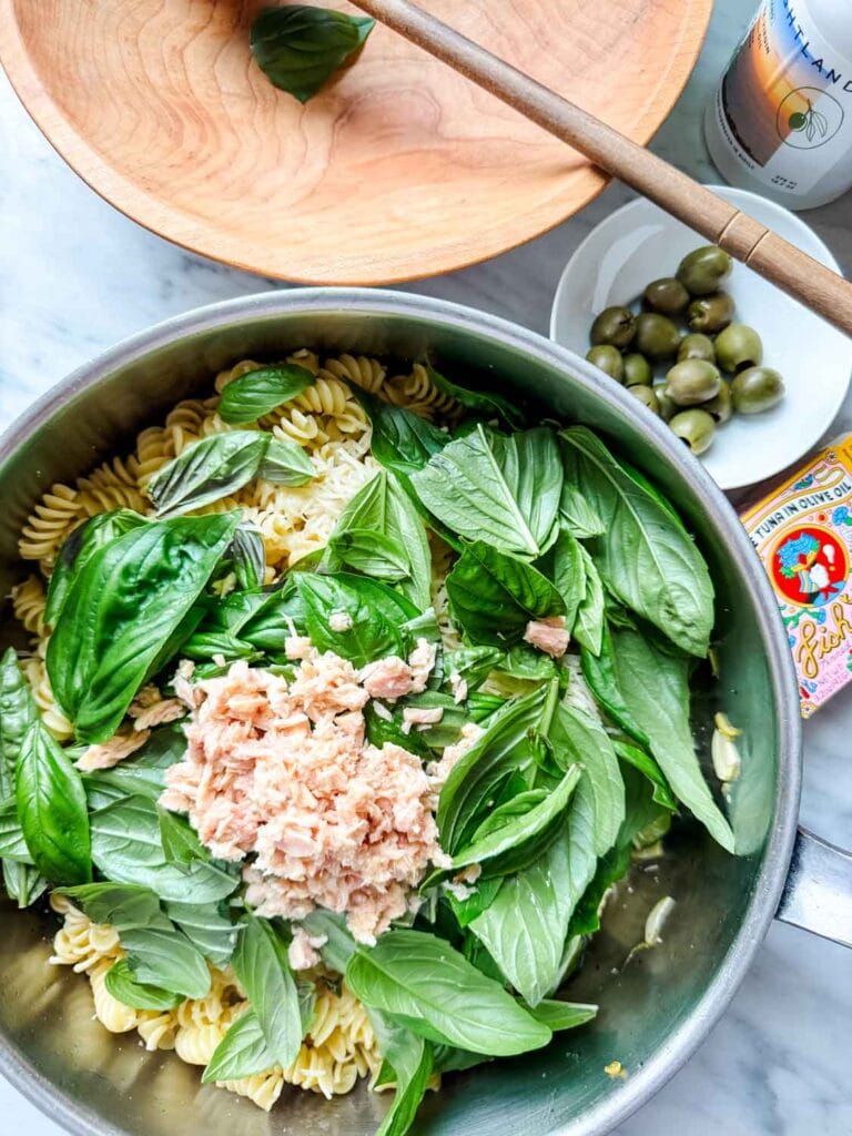 Adding the basil and tinned fish tuna to the pasta in pan.