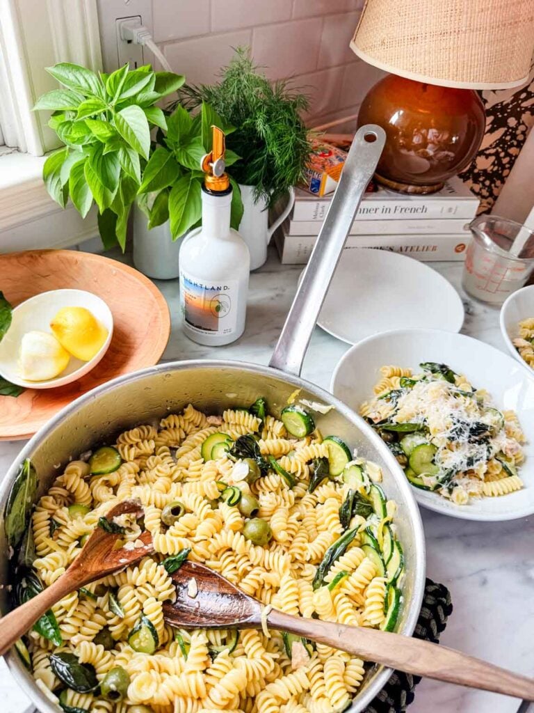 Pasta in pan, with spoons, bowls of pasta.