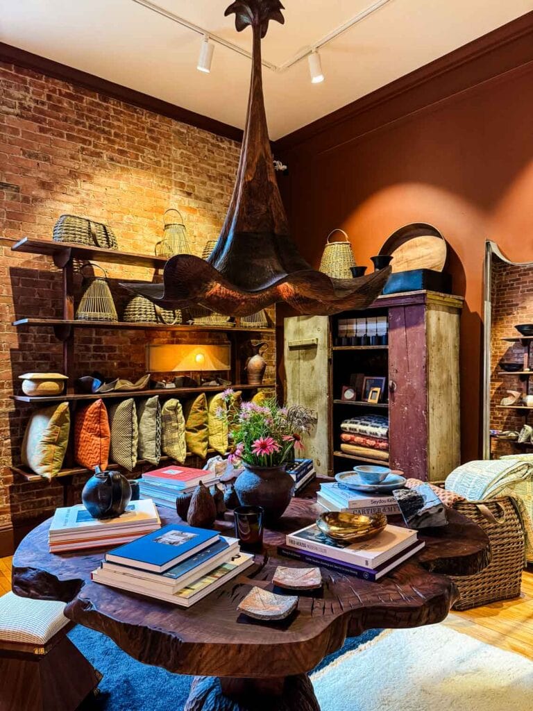 Organic looking table with tulip style pendant, books, pillows on display against brick wall.