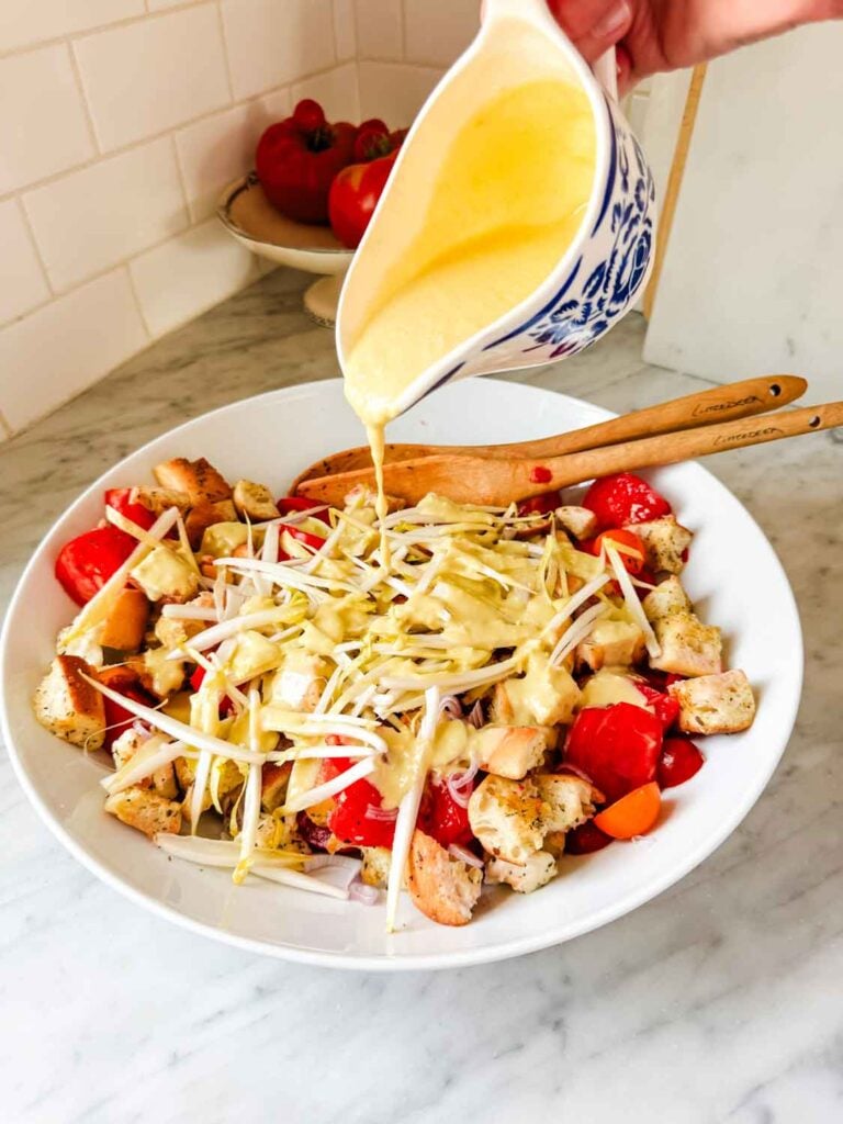 Caesar dressing is drizzled over the baguette croutons, chopped tomatoes, endives, shallots and are ready for mixing.