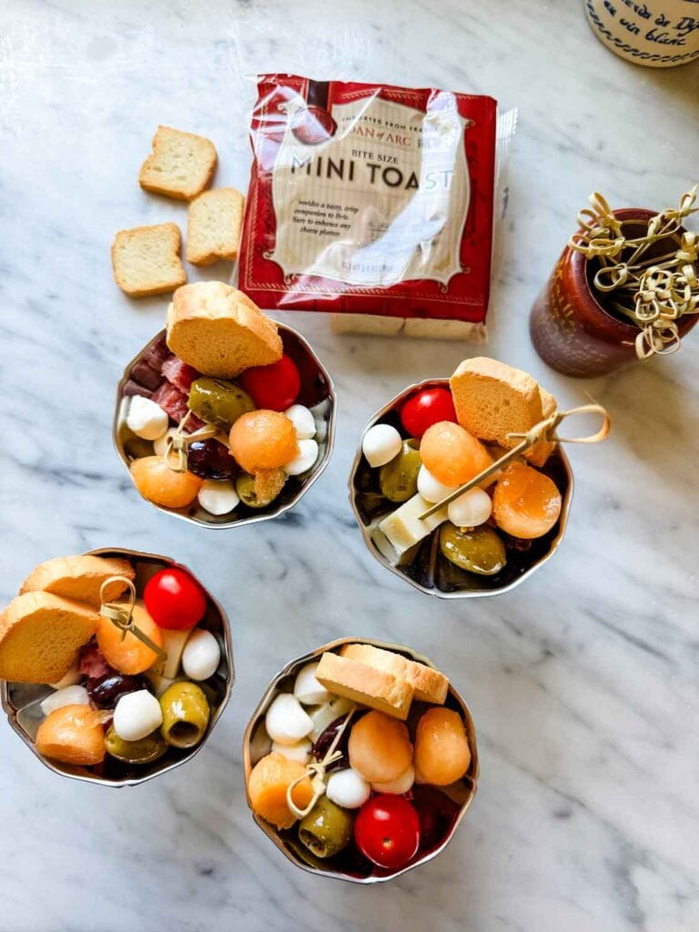 Charcuterie in small stainless dishes with package of mini toasts.