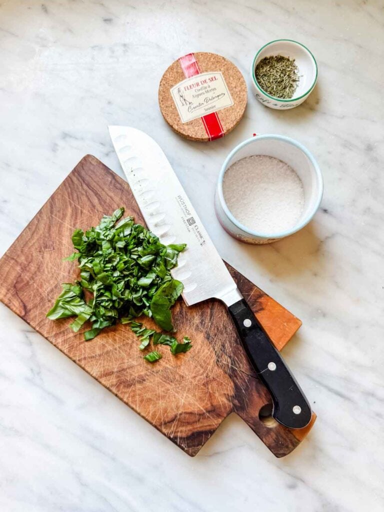 Chopped fresh basil on cutting board with salt and small dish of herbs.