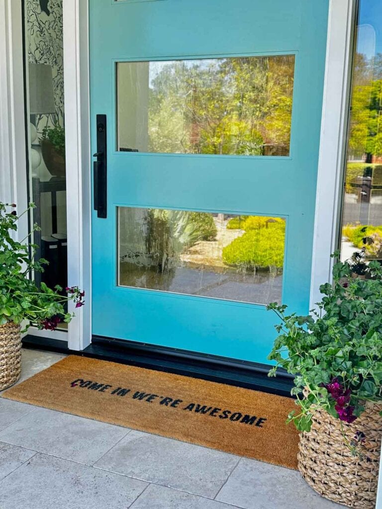 A turqouise front door with glass, and a door mat that says; come in we're awseome,
