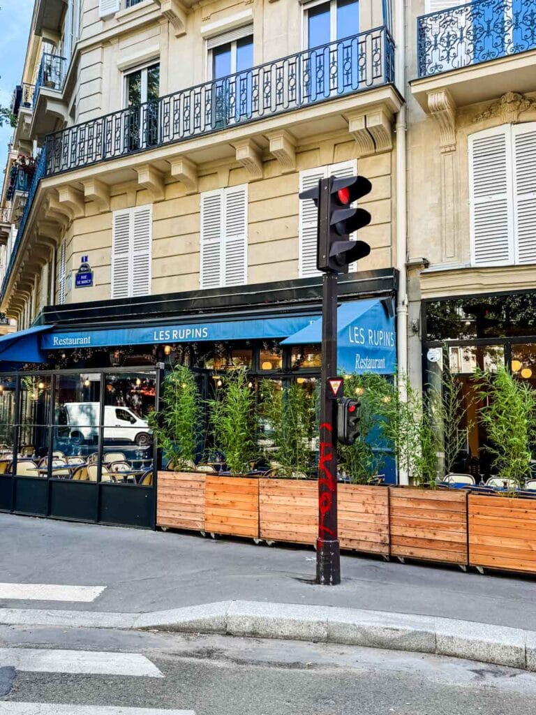 Planters with small trees line the side walk next to the outside dining area at Les Rupins in Paris.