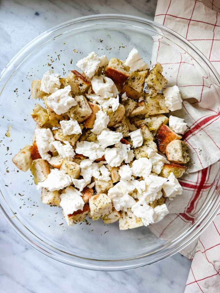 Cubed baguette and Halloumi are being mixed in a large glass bowl before going into the oven.