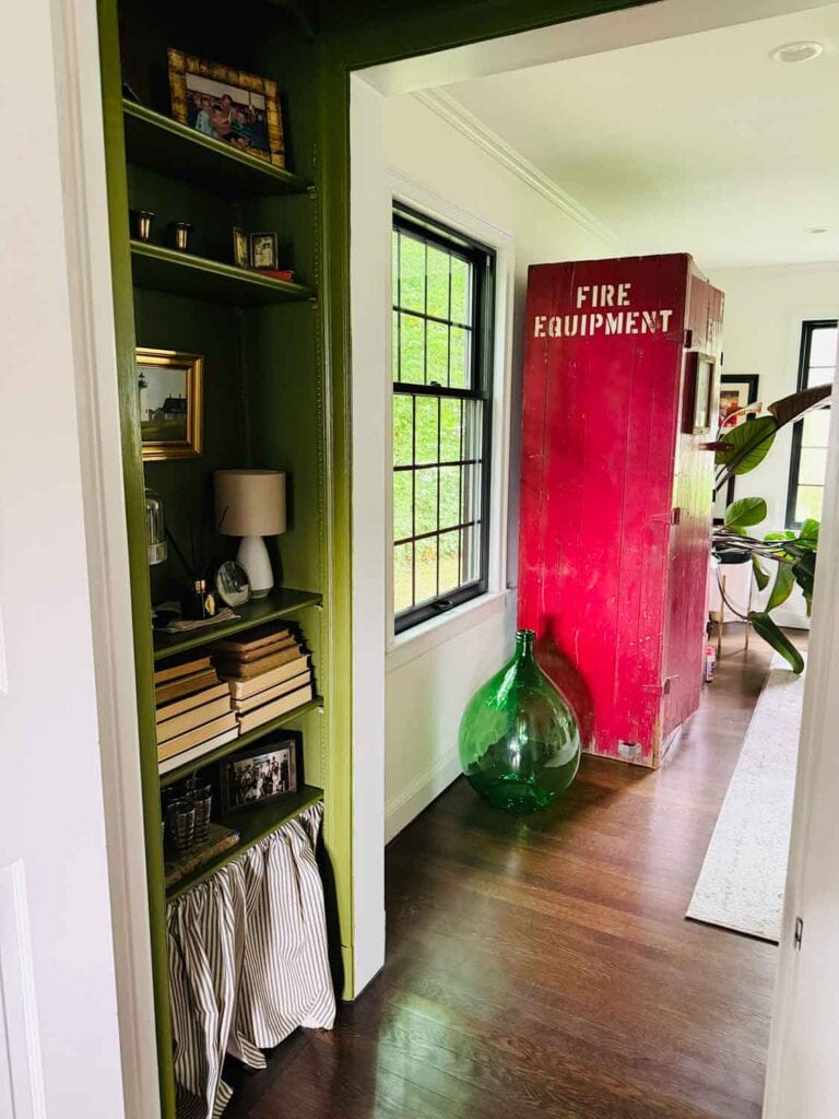 Red fire equipment locker in a living room with glass bottle.