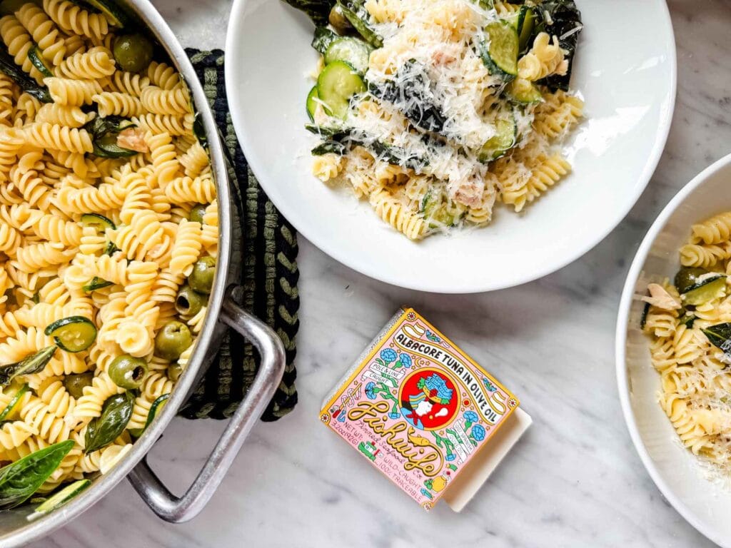 Pasta in white bowls, pan, box of tinned fish tuna.