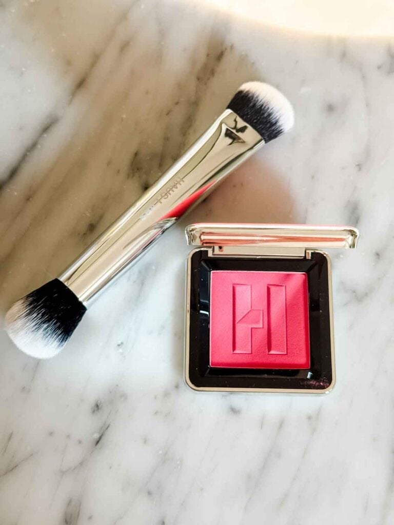 A dual-ended brush with blush powder from Haus Labs is sitting on a bathroom counter.