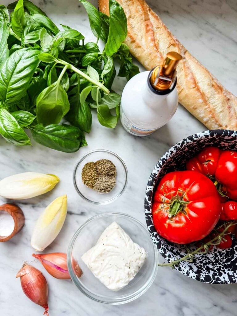 Baguette, fresh tomatoes, basil, dried herbs, endives, shallots, and Halloumi are ready for making Panzanella salad.