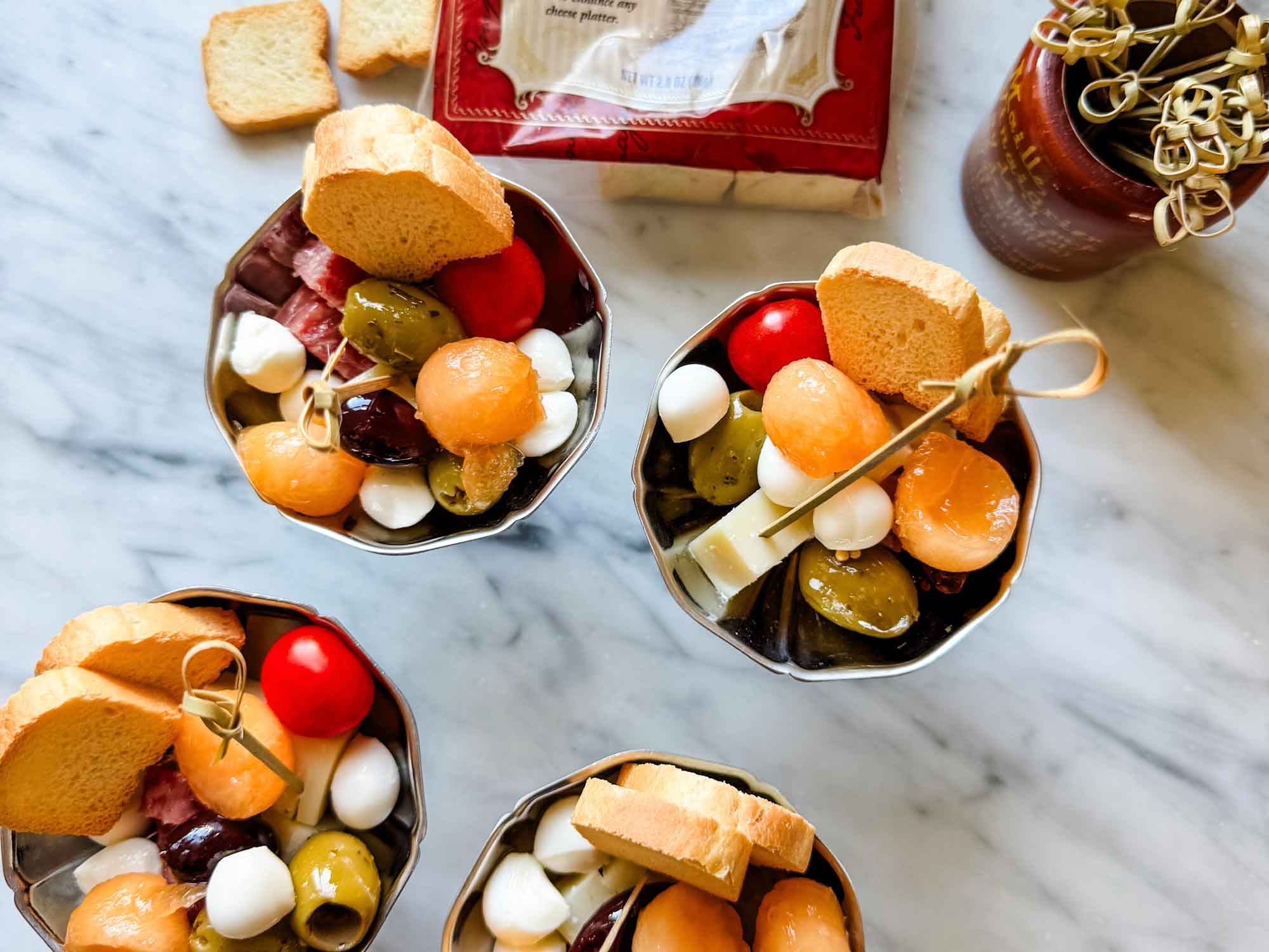 Charcuterie in small stainless dishes with package of mini toasts.