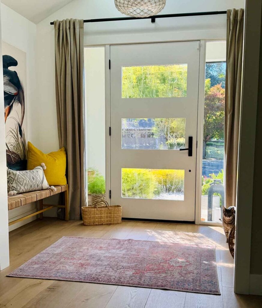 Partial glass front door, baket, rug, bench with pillows.