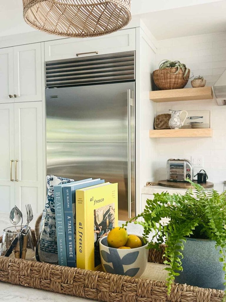 Subzero refriegerator, rattan tray wiith small bowl of lemons, cookbooks, fern.