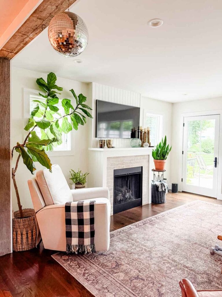 White chair with black and white throw, plant, tv over fireplace. 
