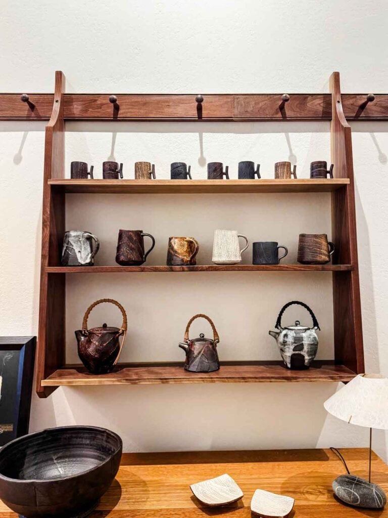 Mugs and tea pots on wood display wall shelf.
