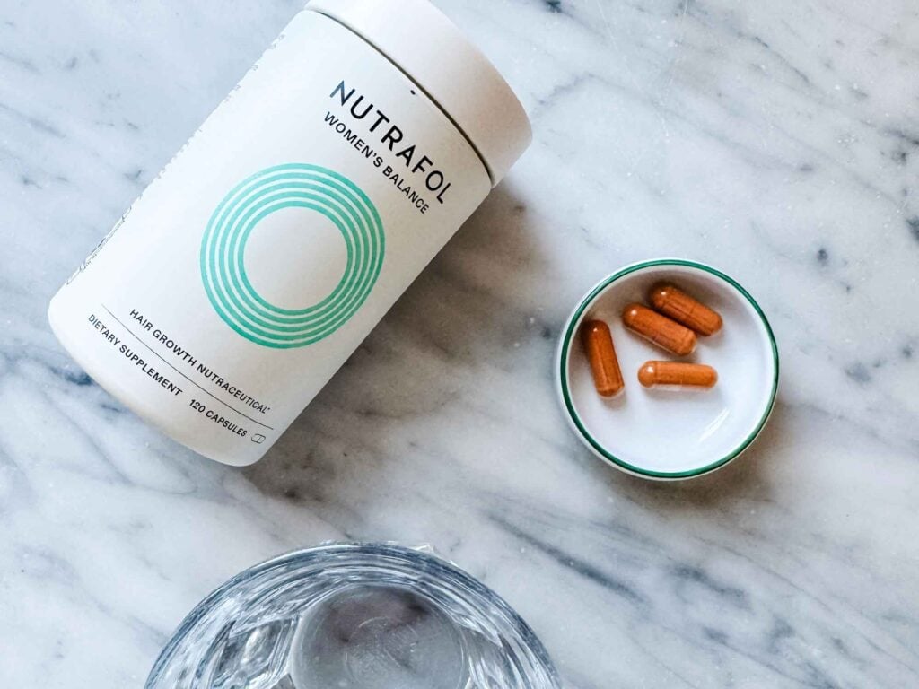Small dish with 4 Nutrafol capsules, jar, glass of water,