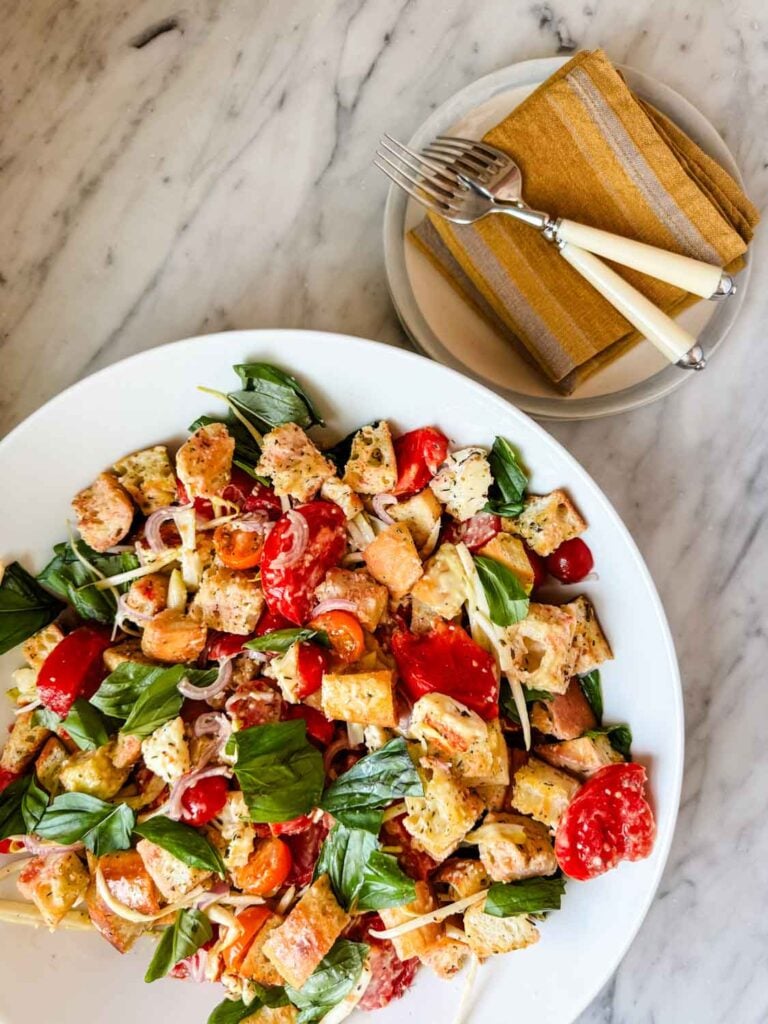 Panzanella salad with homemade Caesar dressing is topped with fresh torn basil leaves and ready for serving.