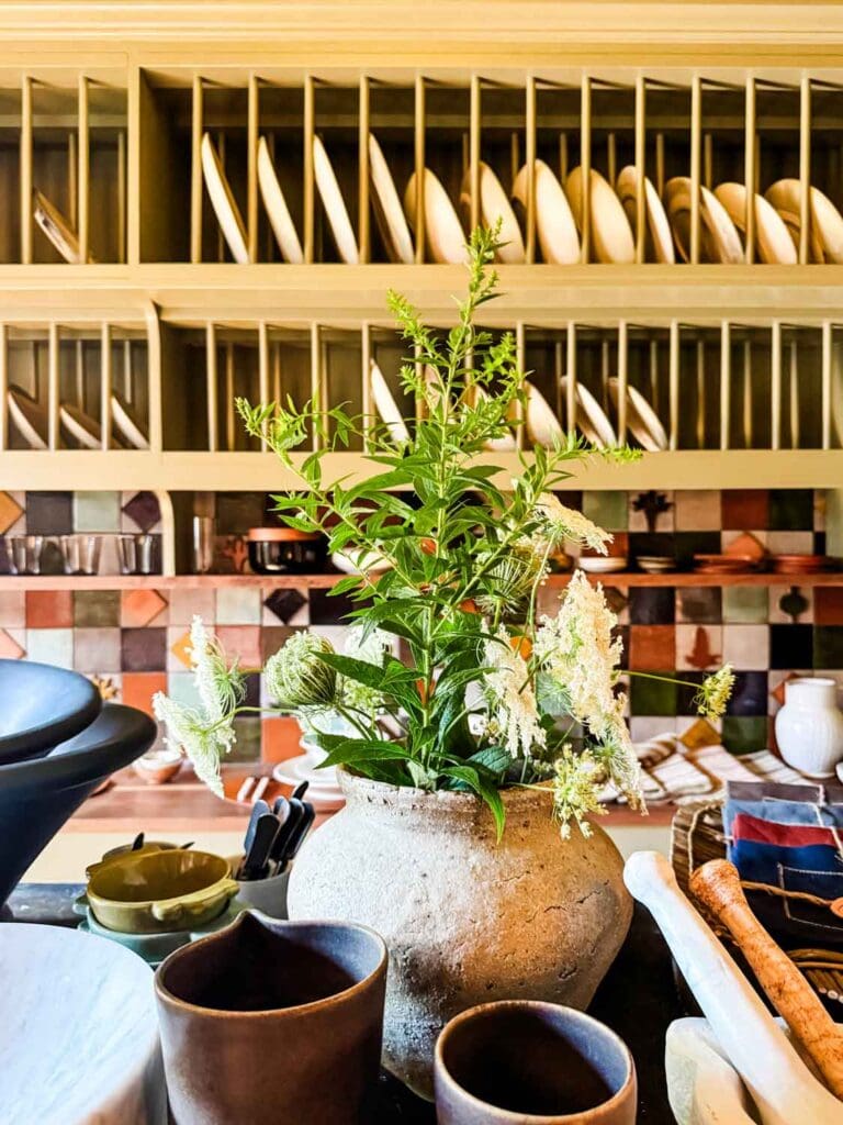 Wall wtih shelf rack to hold plates, vase with wild flowers.