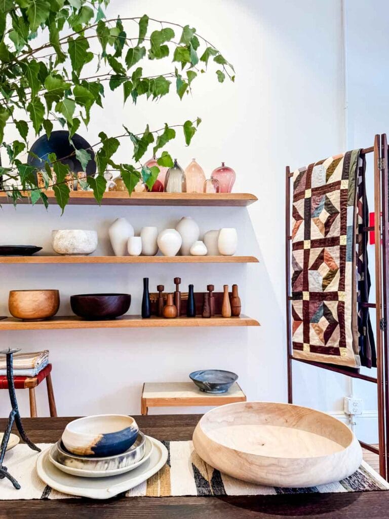 Quilt on display rack, open shelving with wood, cermaic vases, objects.