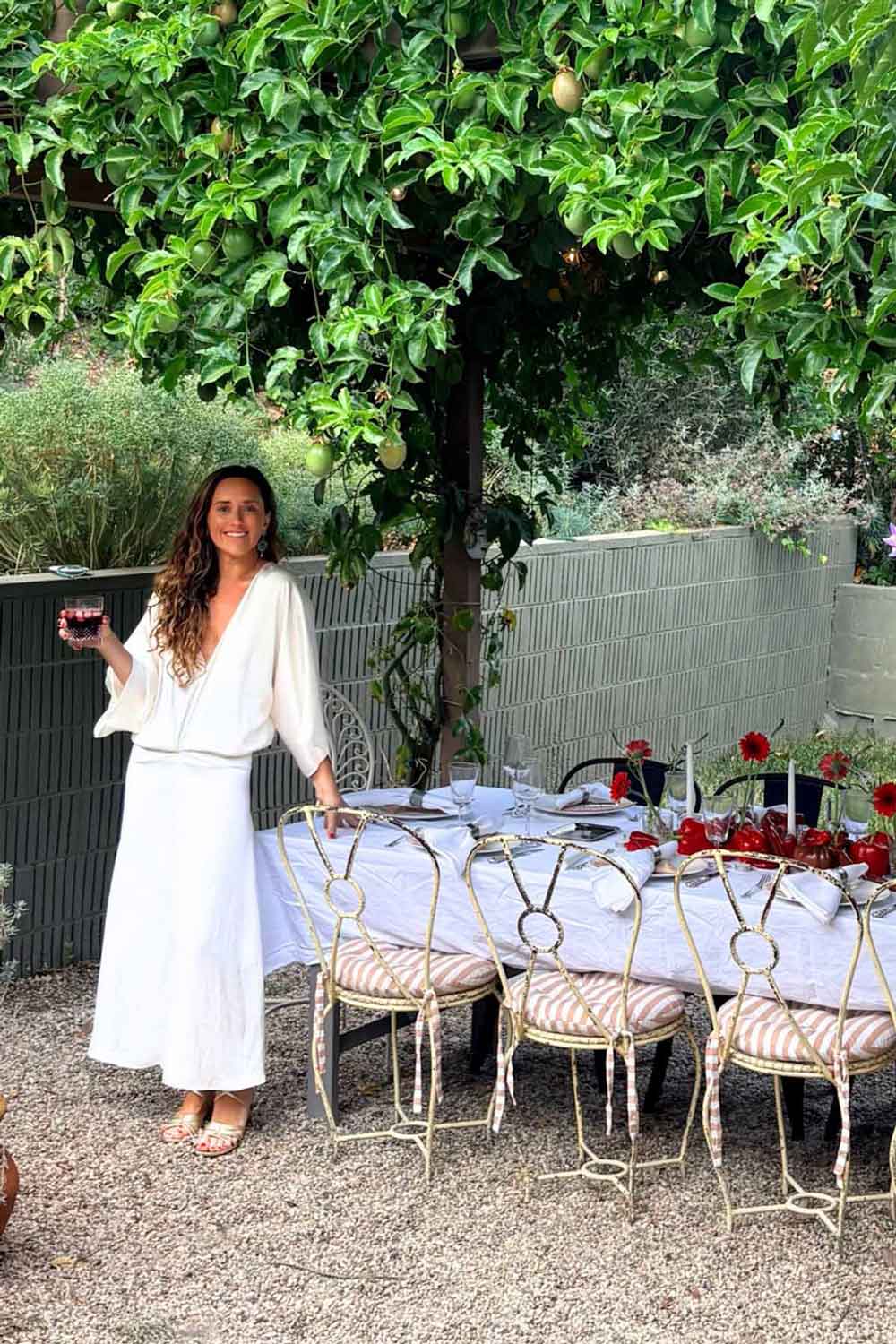 Young woman holding a drink beside a beauitful tablescape under the trees.