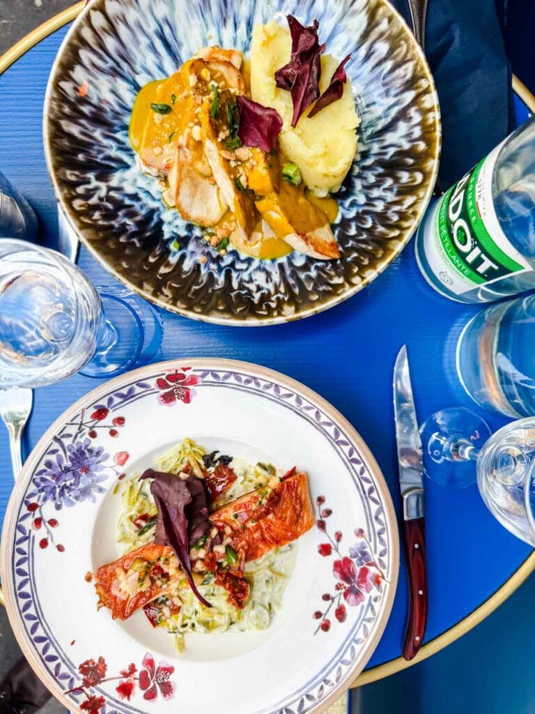 Grilled salmon and stayed chicken with crushed potatoes are served next to a glass of wine and a bottle of sparkling water at Les Rupins.