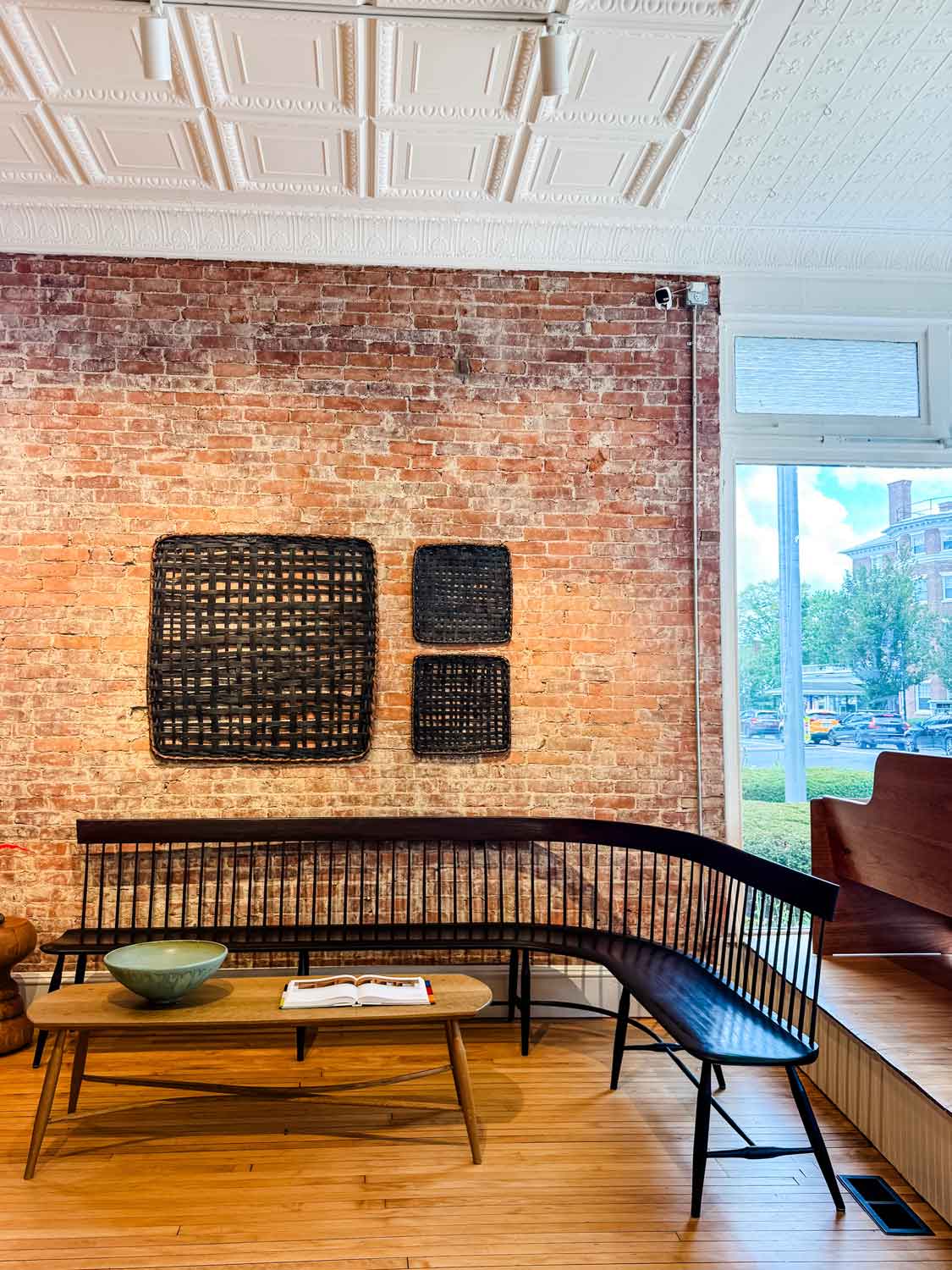 Large wooden curved shaker style bench with baskets displayed on brick wall above. Wood floors and coffee tablwe with green bowl.
