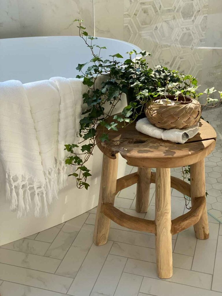 Small wood stool with a plant beside a freestanding tub.