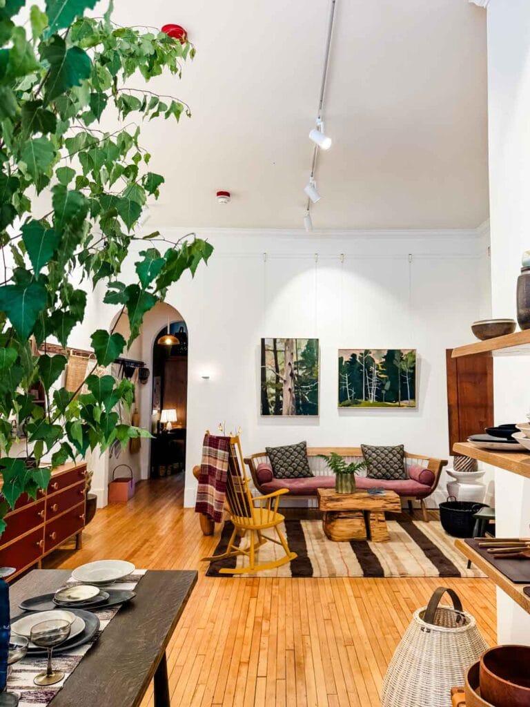 Design shop with large vase with tree branches, art, furniture, wood floors.