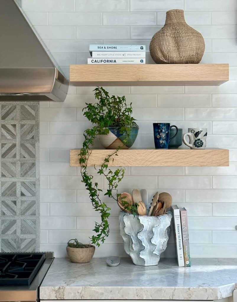 Open shelving in kitchen with mug collection, planter with fern, vase with a ruffle design holding wooden utensils.