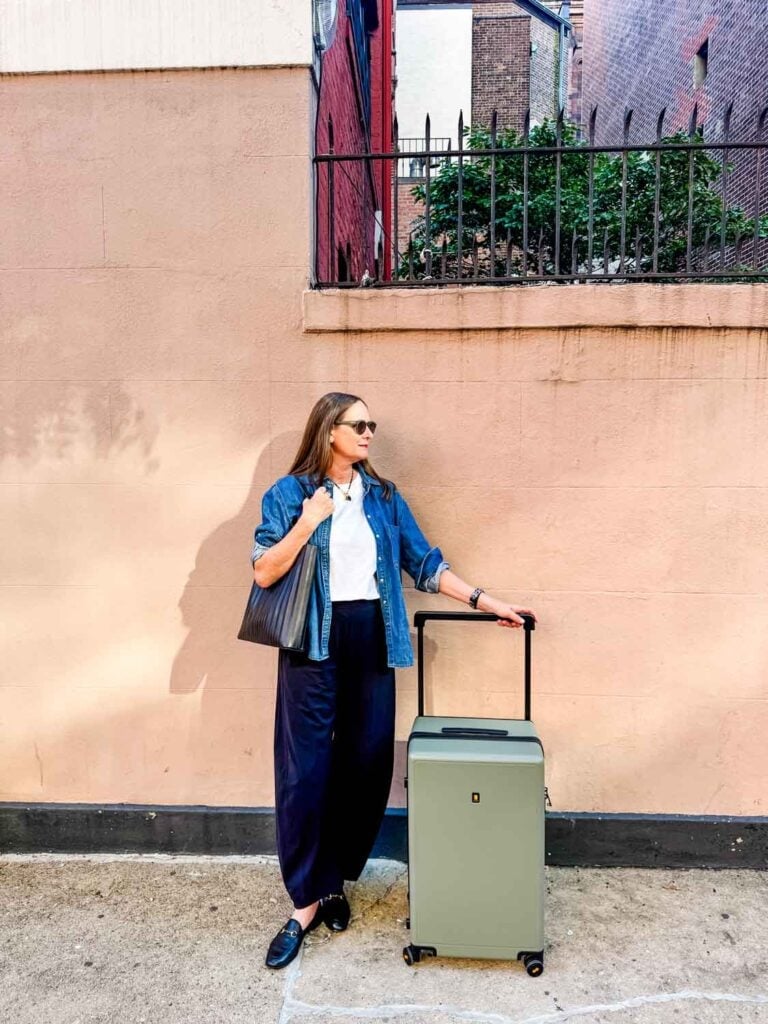 A woman traveling with a Level8 suitcase is standing in front of a pink wall.