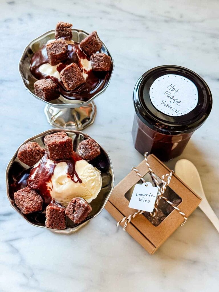 Stainless coupes with hot fudge sundaes with brownie bites, jar of hot fudge labeled.