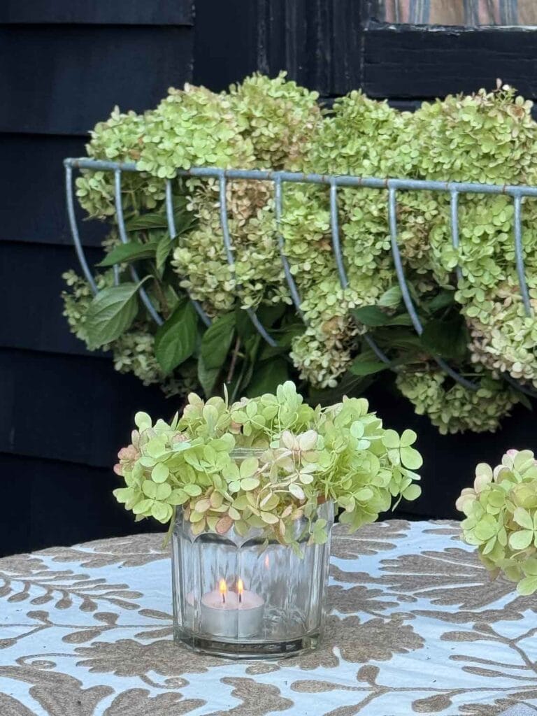A flower crown votive is burning on the table. Behind is a flower box full of extra Hydrangea flowers.