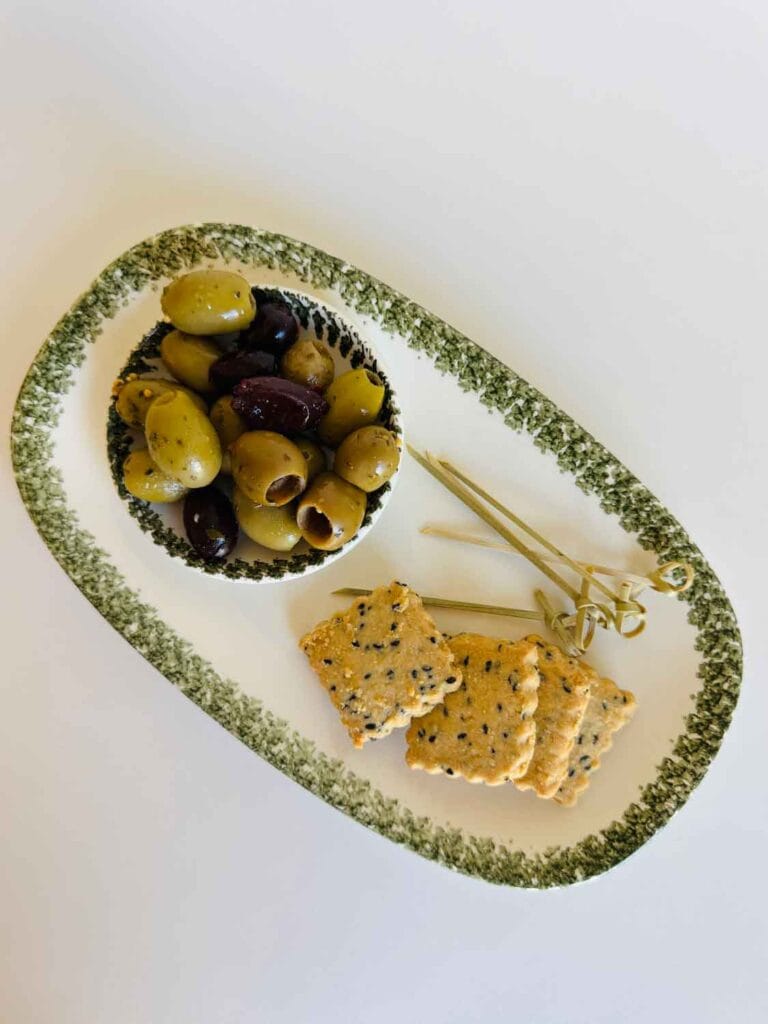 Gien appetizer dish and small bowl of olives beside crackers. 