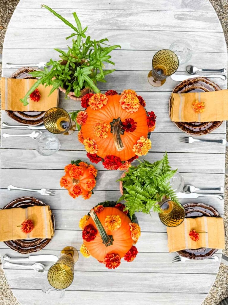 A tablescape with polka-dot pumpkins on galvanized cake stands, plants in terracotta pots, brown plates with gold napkins, and a single marigold on the napkin.