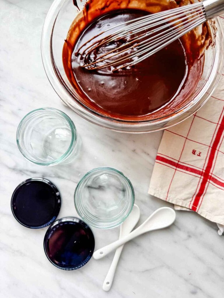Hot fudge in glass mixing bowl with small jars, blacklids and porcelain spoons. 